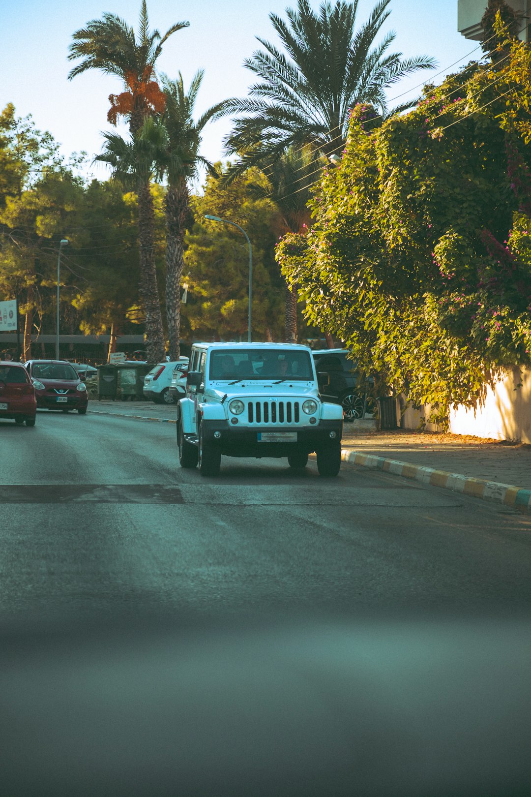 A white jeep driving down a street next to palm trees